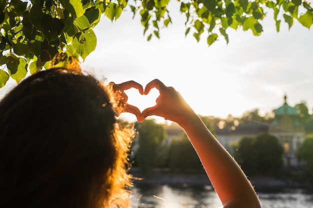 Manos de mujer mostrando la forma de un corazón en la puesta del sol joven viaje solo amor concepto