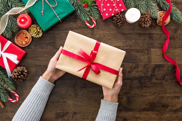 Manos de mujer mostrando regalo de Navidad en mesa de madera