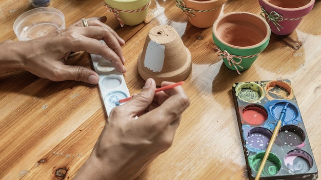 Manos de una mujer mulata latina pintando ollas de barro para plantar plantas suculentas