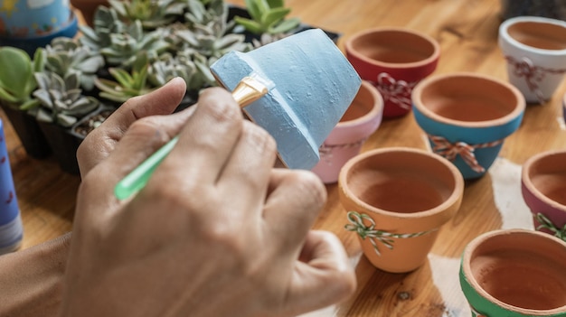 Manos de una mujer mulata latina pintando ollas de barro para plantar plantas suculentas