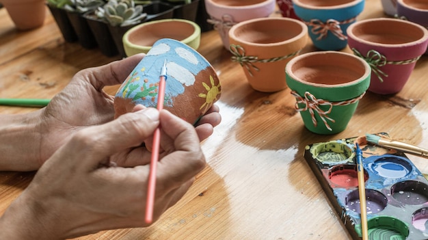 Manos de una mujer mulata latina pintando ollas de barro para plantar plantas suculentas