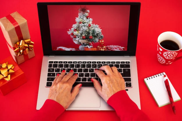 Manos de mujer navegando en la computadora portátil en Navidad con fondo rojo con regalos de Navidad y taza de té