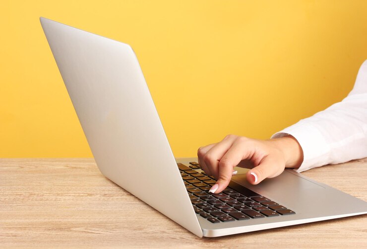 Foto las manos de una mujer de negocios escribiendo en una computadora portátil en un primer plano de fondo amarillo