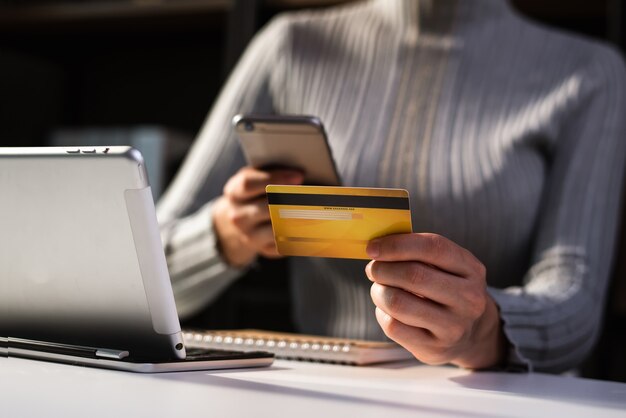 Manos de mujer de negocios con smartphone y sosteniendo tarjeta de crédito sentado. Concepto de pagos de compras en línea.