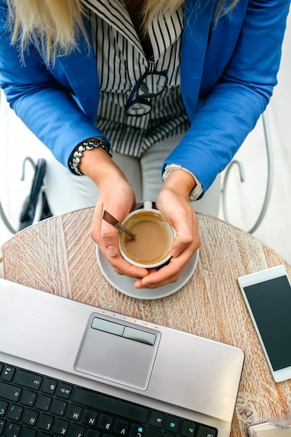 Manos de mujer de negocios sosteniendo una taza de café mientras mira la computadora portátil