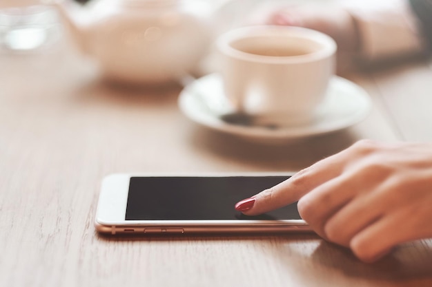 Manos de mujer de negocios usando un teléfono inteligente y una taza de café