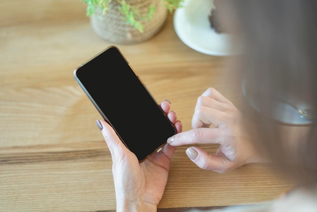 Manos de mujer con pantalla negra en blanco de teléfono inteligente Vista sobre el hombro Mujer en café durante el desayuno