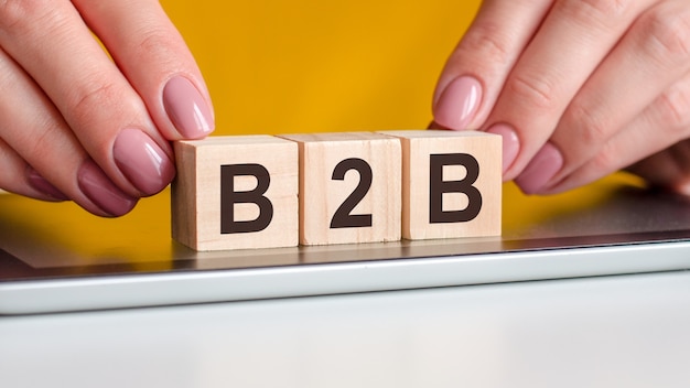 Manos de mujer pone unos bloques de madera con las letras b2b sobre la superficie negra del bloc de notas. Se puede utilizar para negocios, marketing, educación, concepto.