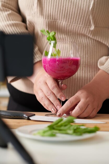 Manos de mujer poniendo un vaso de delicioso batido rojo con rúcula que preparó para el desayuno