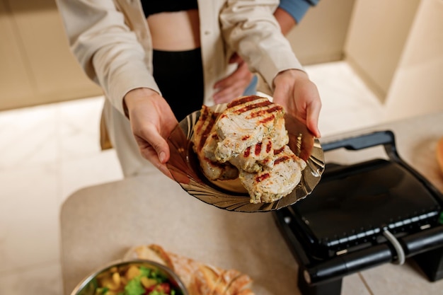 Las manos de la mujer preparan un delicioso bistec de carne jugosa en una parrilla eléctrica sobre una mesa de madera Humo en la cocina de la casa