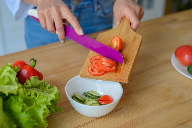 Manos de mujer de primer plano para picar verduras de pepino con un cuchillo