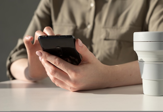 Manos de mujer primer plano sosteniendo teléfono mujer sentada en la mesa y el uso de gadget para el trabajo de comunicación edu...