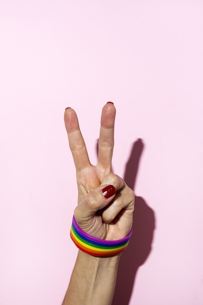 Manos de mujer con pulsera LGBT sobre fondo rosa