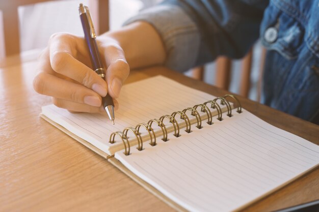 Las manos de la mujer que escriben en la libreta espiral colocada en el escritorio de madera.