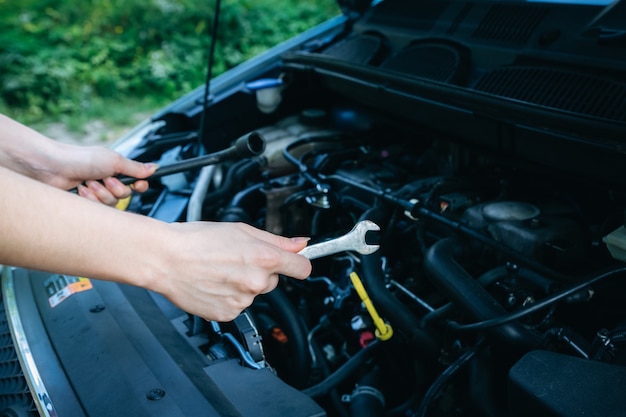 Foto manos de una mujer que está reparando un coche roto.