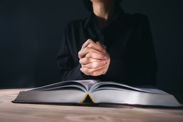 Manos de mujer rezando con una Biblia en una habitación oscura