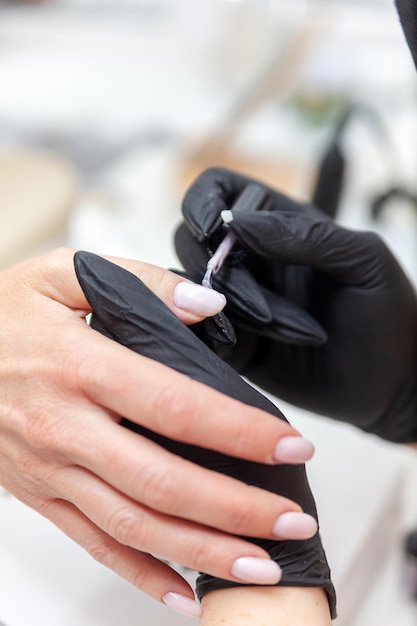 Manos de mujer en un salón de uñas que el maestro de manicura cubre las uñas con una capa base de esmalte de gel