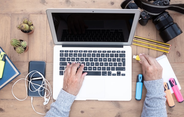 Manos de mujer senior trabajando en el portátil al aire libre en una mesa de madera escribiendo el teclado