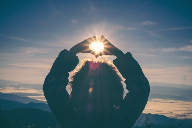 Manos de mujer en símbolo del corazón en forma de amanecer