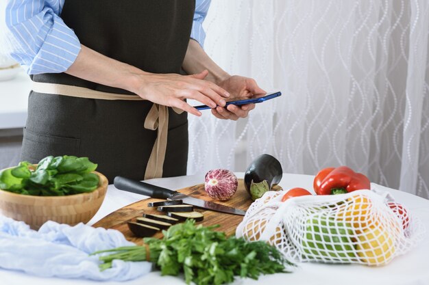 Manos de mujer con smartphone en cocina cocinar verduras cocinar en casa concepto