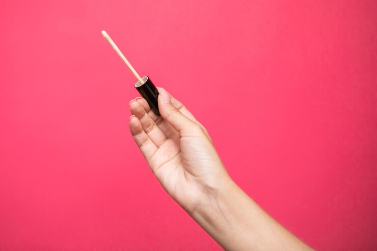 Manos de mujer sosteniendo aplicador de corrector aislado sobre fondo rosa