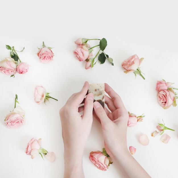 Manos de mujer sosteniendo la barra de jabón natural floral con flores sobre superficie blanca