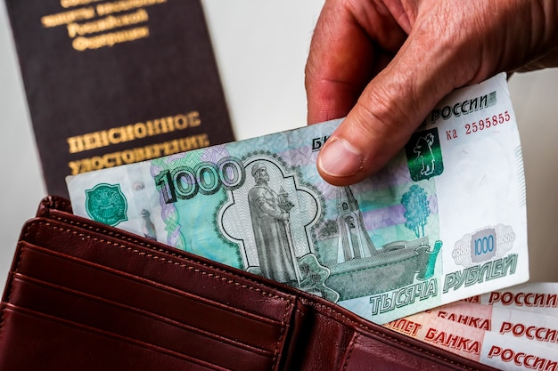 Manos de mujer sosteniendo la billetera con rublos rusos certificado de pensión rusa en segundo plano.