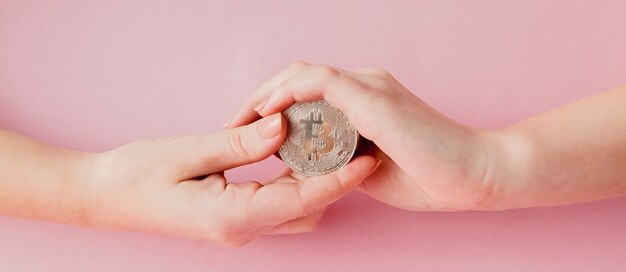 Manos de mujer sosteniendo bitcoin en rosa, símbolo de dinero virtual.