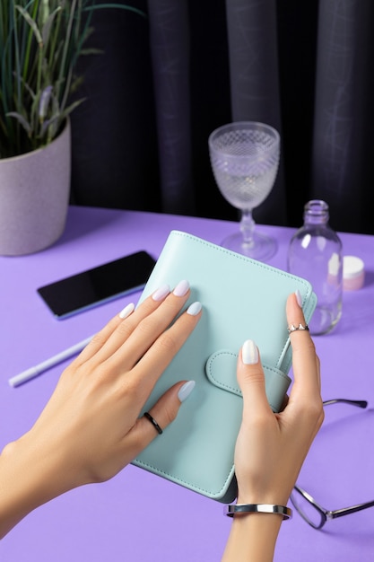 Manos de mujer sosteniendo el bloc de notas sobre la mesa violeta. Accesorios femeninos de verano