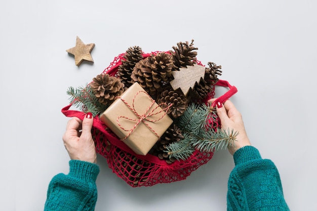 Manos de mujer sosteniendo una bolsa de malla con conos de decoración de cero residuos de Navidad y ramas de abeto para un diseño hecho a mano