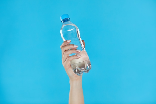 Manos de mujer sosteniendo una botella de agua en azul.