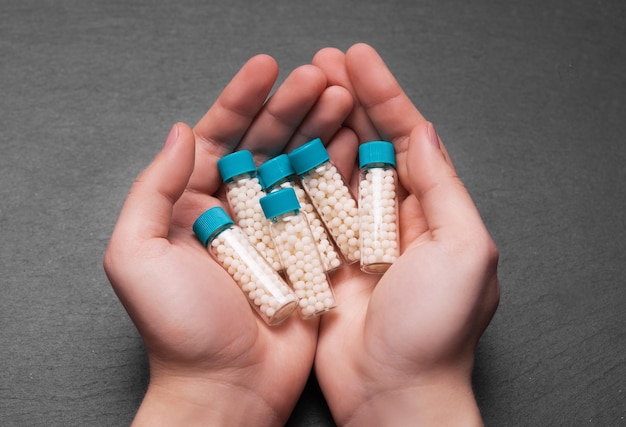 Manos de mujer sosteniendo una botella con pastillas homeopáticas sobre fondo negroxA