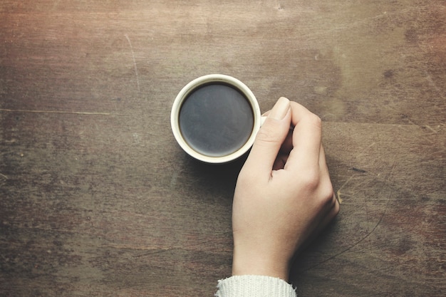 Manos de mujer sosteniendo café en la mesa de madera