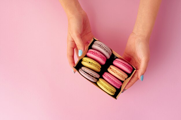 Manos de mujer sosteniendo caja con coloridas galletas de macarrón