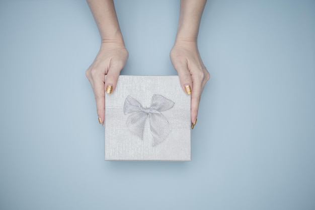 Manos de mujer sosteniendo caja de regalo con fondo azul.