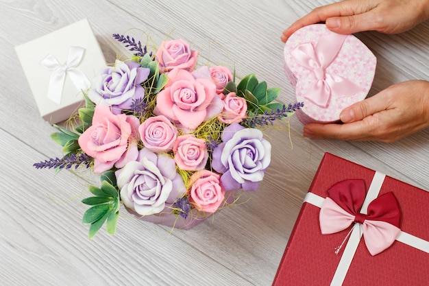 Manos de mujer sosteniendo una caja de regalo en forma de corazón con jabón en forma de rosas