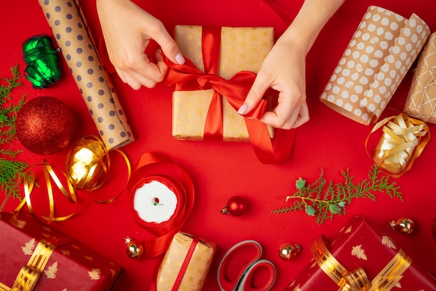 Manos de mujer sosteniendo caja de regalo de Navidad sobre un fondo rojo.