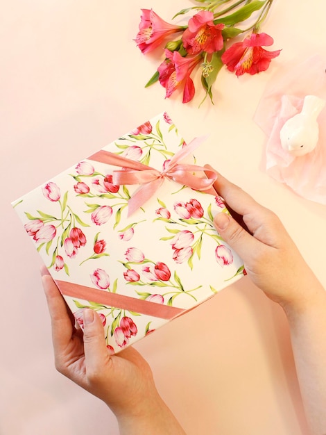 Manos de mujer sosteniendo caja de regalo sobre fondo rosa pastel Estilo plano laico