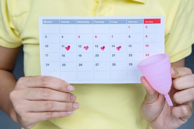 Foto las manos de la mujer sosteniendo un calendario y un vaso higiénico