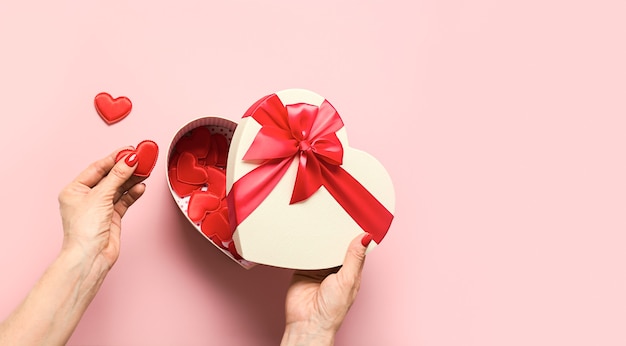 Manos de mujer sosteniendo corazones rojos de la caja de regalo del día de San Valentín en rosa