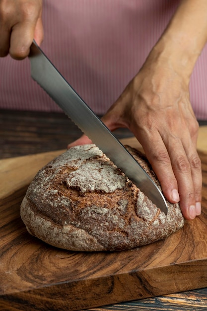 Manos de una mujer sosteniendo y cortando un pan rústico de masa fermentada con un cuchillo foto de archivo