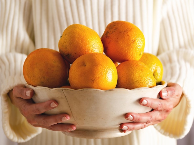 Manos de una mujer sosteniendo un cuenco lleno de naranjas