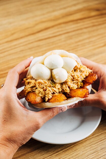 Foto manos de una mujer sosteniendo deliciosa arepa venezolana rellena de pollo, plátano frito y huevos de corniz