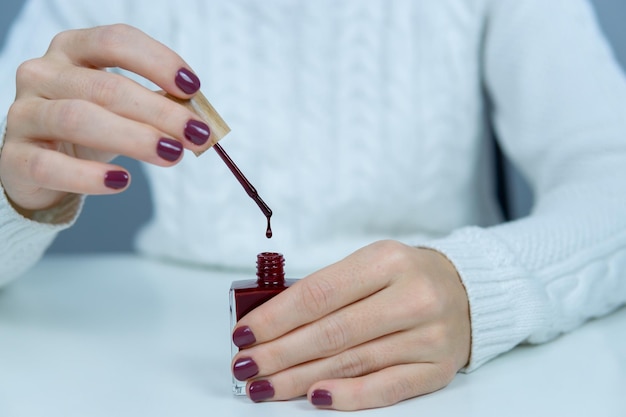 Manos de mujer sosteniendo un esmalte de uñas y un cepillo de esmalte de uñas mientras cae una gota sobre él