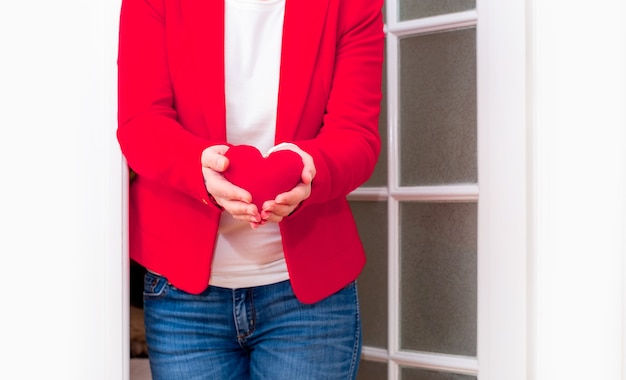 Manos de mujer sosteniendo gran corazón rojo del día de San Valentín cerca de la puerta blanca.