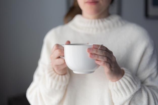 Manos de mujer sosteniendo una gran taza blanca de té caliente