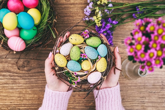 Manos de mujer sosteniendo huevo de pascua pintado en un nido pequeño imagen tonificada vista superior enfoque selectivo