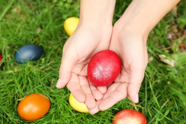 Manos de mujer sosteniendo el huevo de Pascua en la superficie de la hierba verde