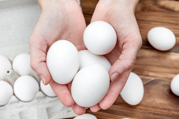 Manos de mujer sosteniendo huevos sobre la mesa con huevos y contenedor de cartón