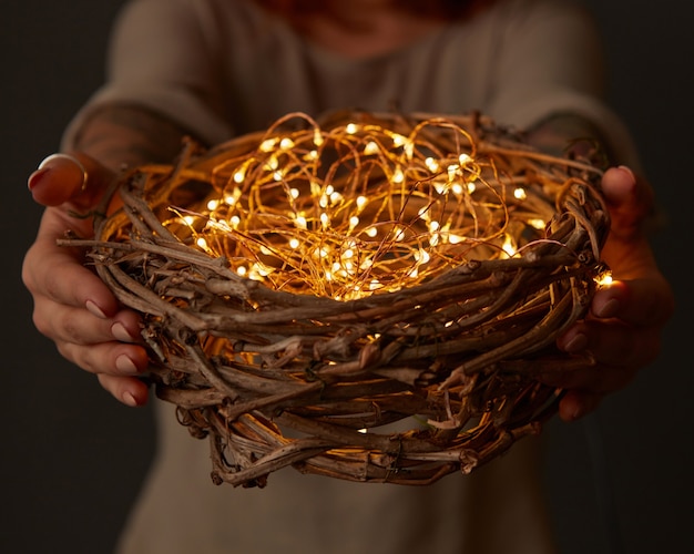 Manos de mujer sosteniendo un nido con luces sobre fondo oscuro. Inspiración para las vacaciones de Pascua